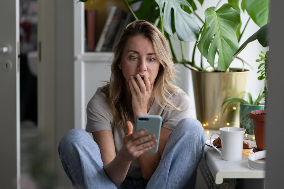 A woman sitting and looking at her phone in shock