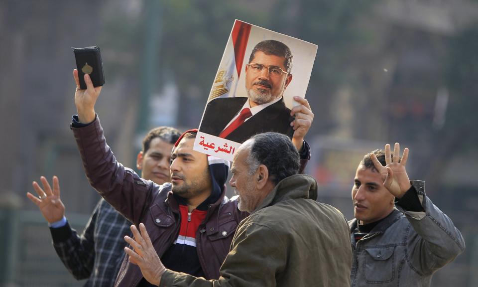 Supporters of the Muslim Brotherhood and ousted Egyptian President Mohamed Mursi hold a copy of the Koran and Mursi's picture at Talaat Harb Square, in Cairo, January 25, 2015. A bomb wounded two Egyptian policemen in Cairo on Sunday and security forces moved quickly to disperse small protests on the anniversary of the popular uprising that toppled autocrat Hosni Mubarak in 2011, officials said. REUTERS/Mohamed Abd El Ghany (EGYPT - Tags: POLITICS CIVIL UNREST)