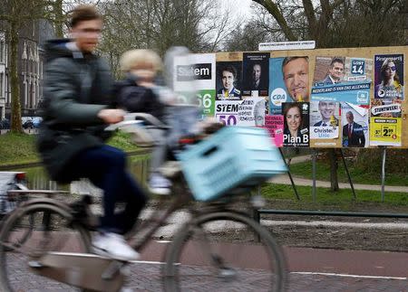 A man and child cycle past an election poster billboard the day before a general election, in Utrecht, Netherlands, March 14, 2017. REUTERS/Michael Kooren