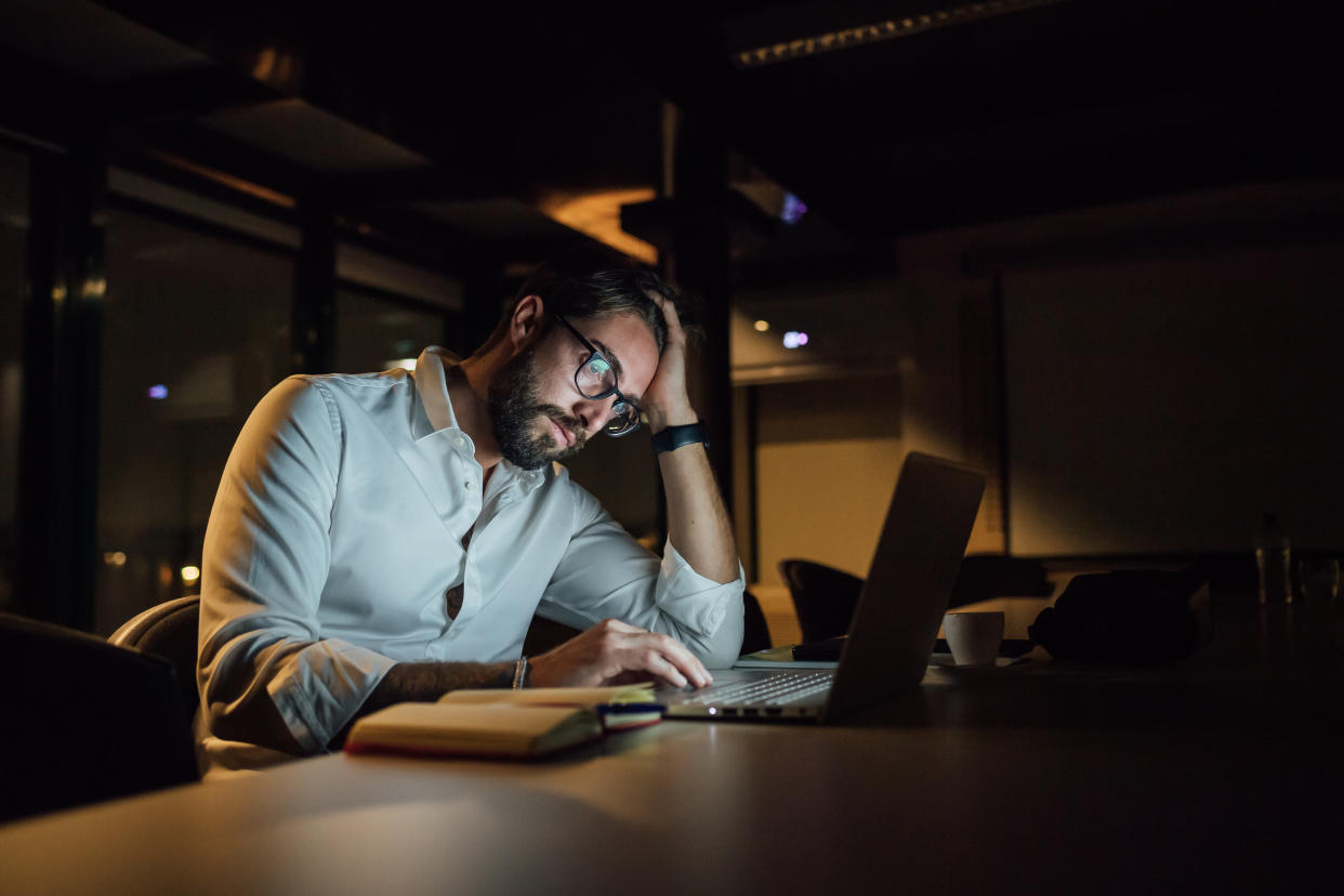 Tired businessman in office at night typing on laptop