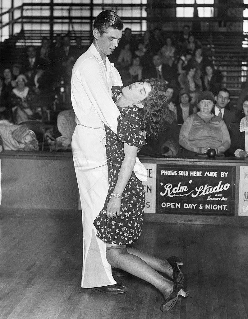 A man holding a sleeping woman as her legs dangle on the dance floor