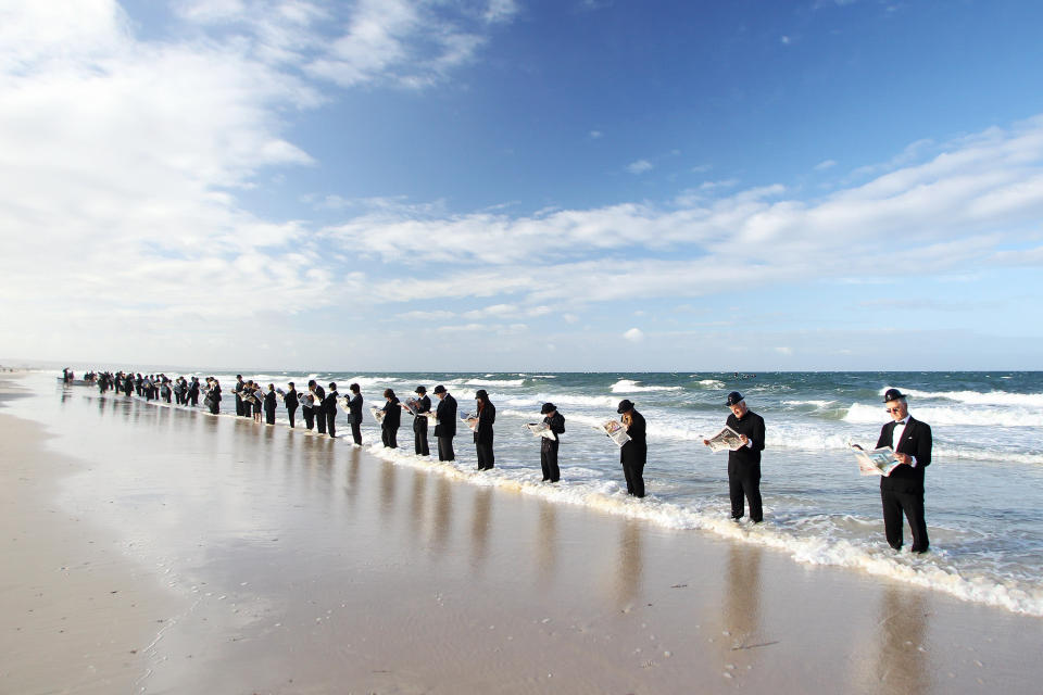 Voluntarios leen el periódico mientras "esperan el bus" en la playa de Henley Beach en Australia. El artista Andrew Baines reclutó 100 voluntarios para participar en esta instalación humana destinada a ilustrar a empleados de una corporación disfrutando de la naturaleza en lugar de esperar en línea para ir al trabajo. (Foto Morne de Klerk/Getty Images)