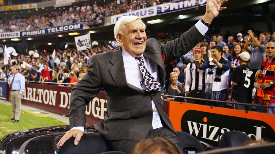 Lou Richards is pictured riding a car in a lap of honour at an AFL game.