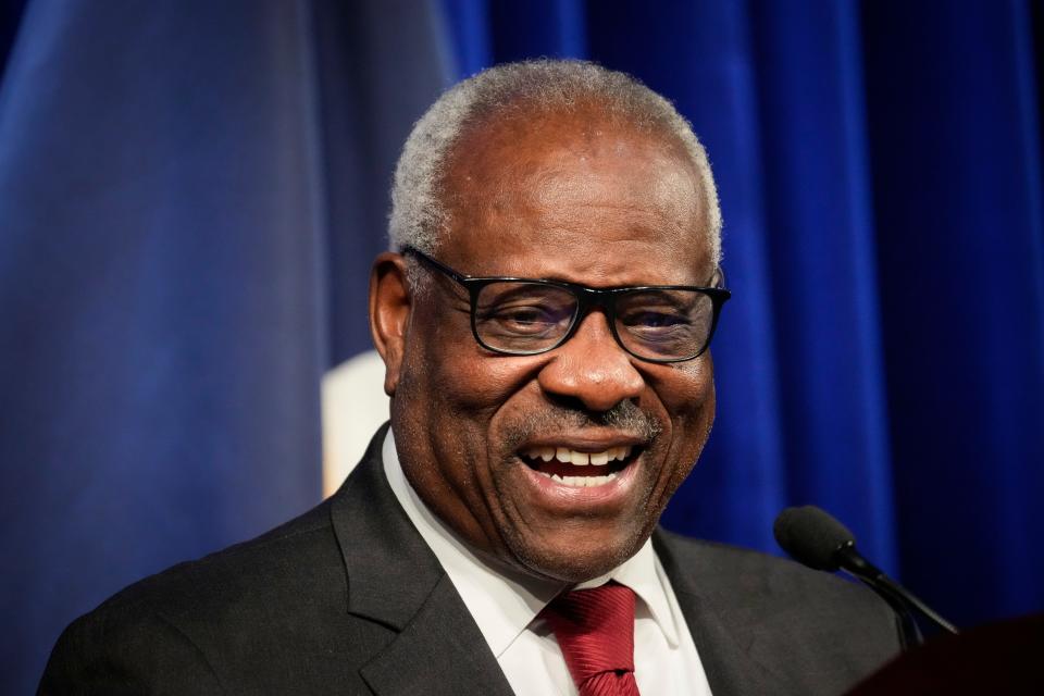 Supreme Court Justice Clarence Thomas standing at a podium and laughing.