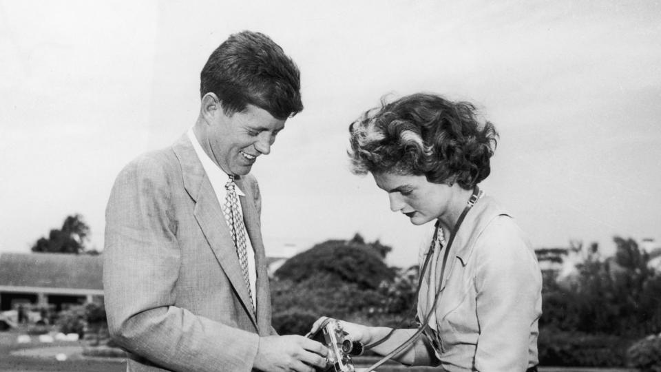 John F Kennedy (1917 - 1963) helping his wife, Jacqueline Bouvier Kennedy (1929 - 1994), adjust a camera in front of their home in Hyannis Port, Massachusetts