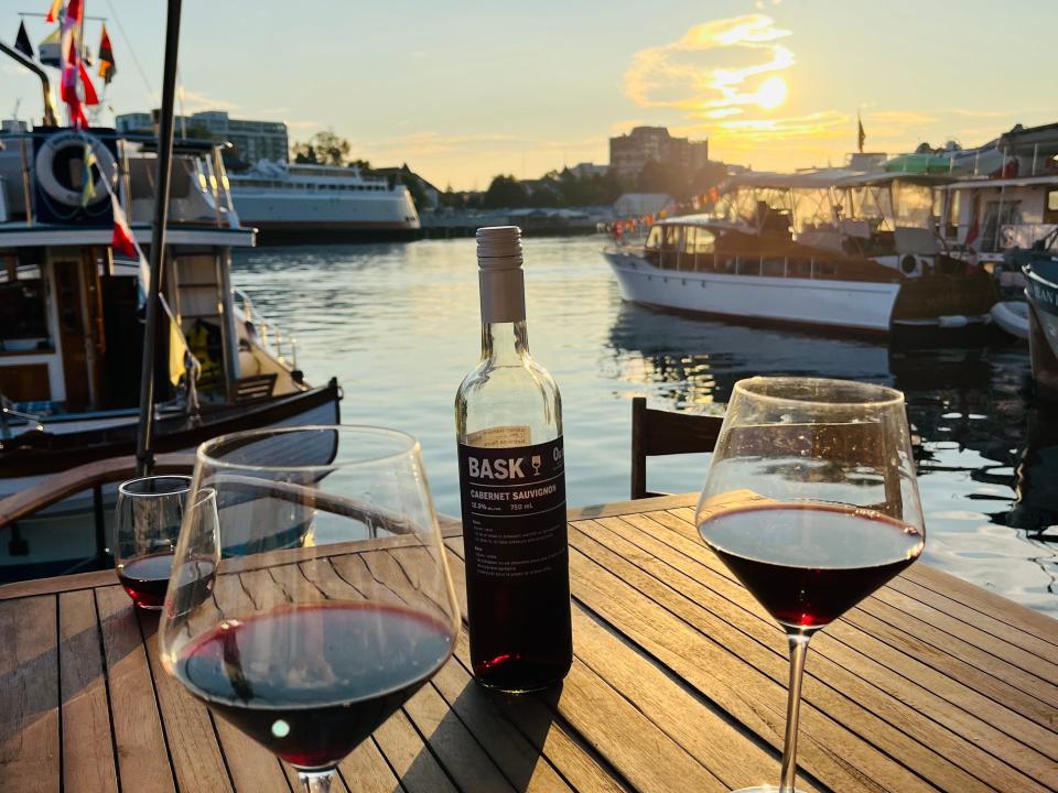 glasses of wine around a bottle on the deck of a boat overlooking the sunset over the water