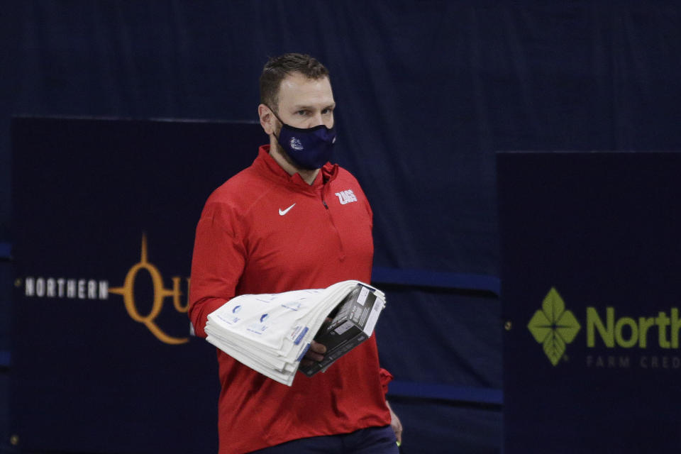 Gonzaga head athletic trainer Josh Therrien carries towels and gloves before an NCAA college basketball game against Pepperdine in Spokane, Wash., Thursday, Jan. 14, 2021. Athletic trainers have been responsible for determining team safety protocols for practices, games and travel. They test athletes and have to be vigilant with contact tracing to prevent outbreaks. Some even make deliveries to those in quarantine. (AP Photo/Young Kwak)