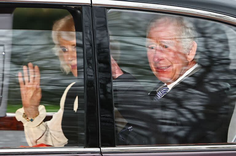 El rey Carlos III de Gran Bretaña y la reina Camilla de Gran Bretaña saludan mientras salen en automóvil desde Clarence House en Londres el 6 de febrero de 2024. (AFP/Henry Nicholls)