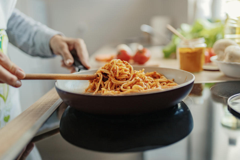 someone tossing spaghetti in sauce in a pan