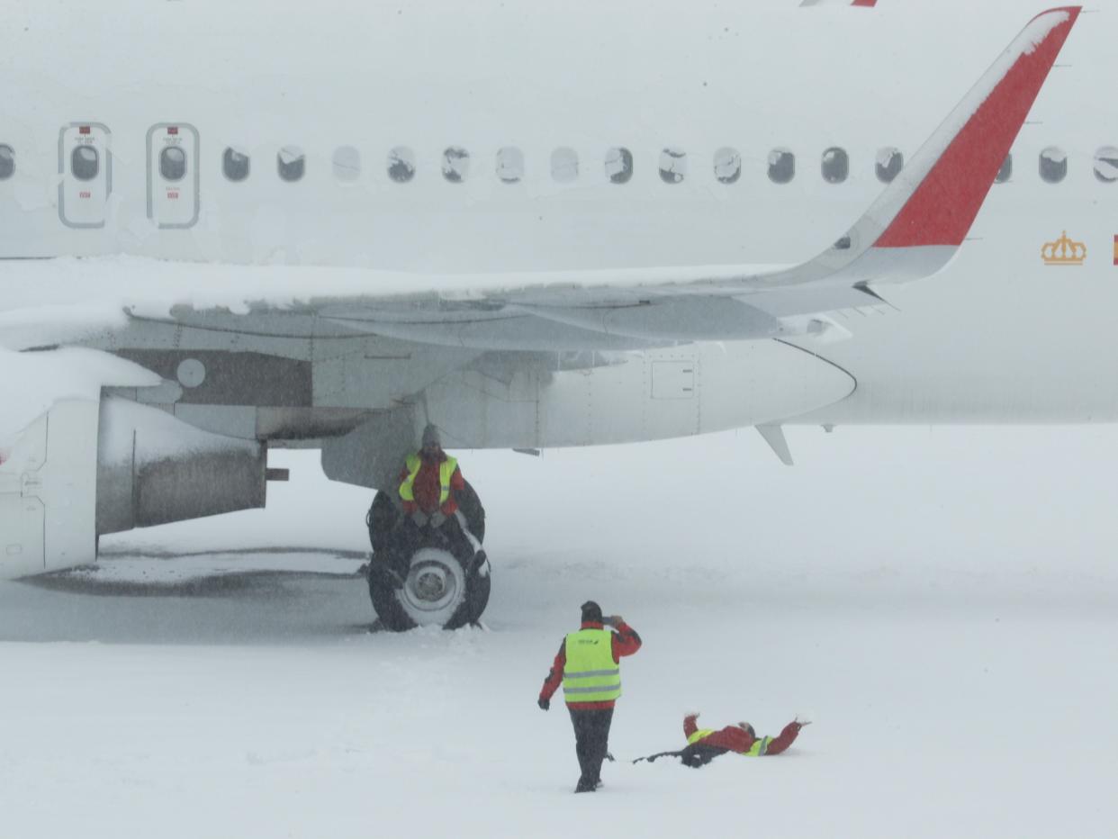 <p>An airport worker sits on the wheel of a parked snow-covered plane as one of his colleague takes a picture of another coworker lying on the snow at Adolfo Suarez Barajas airport, which is suspending flights due to heavy snowfall in Madrid</p> (Reuters)