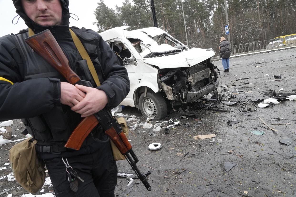 An armed man stands by a damaged vehicle at a checkpoint in Brovary, outside Kyiv, Ukraine, Tuesday, March 1, 2022.