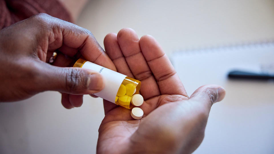 person emptying tablets onto their hand from a bottle