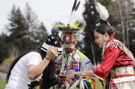 In this photo taken Saturday, April 4, 2020, Tera Baker, left, huddles over a cell phone with her children Wakiyan Cuny, center, and Wicahpi Cuny, all Dakota and Lakota tribal members, during a live streamed powwow from a park near their home in Puyallup, Wash. The largest powwows in the country have been canceled or postponed amid the spread of the coronavirus. Tribal members have found a new outlet online with the Social Distance Powwow. They're sharing videos of colorful displays of culture and tradition that are at their essence meant to uplift people during difficult times. (AP Photo/Elaine Thompson)