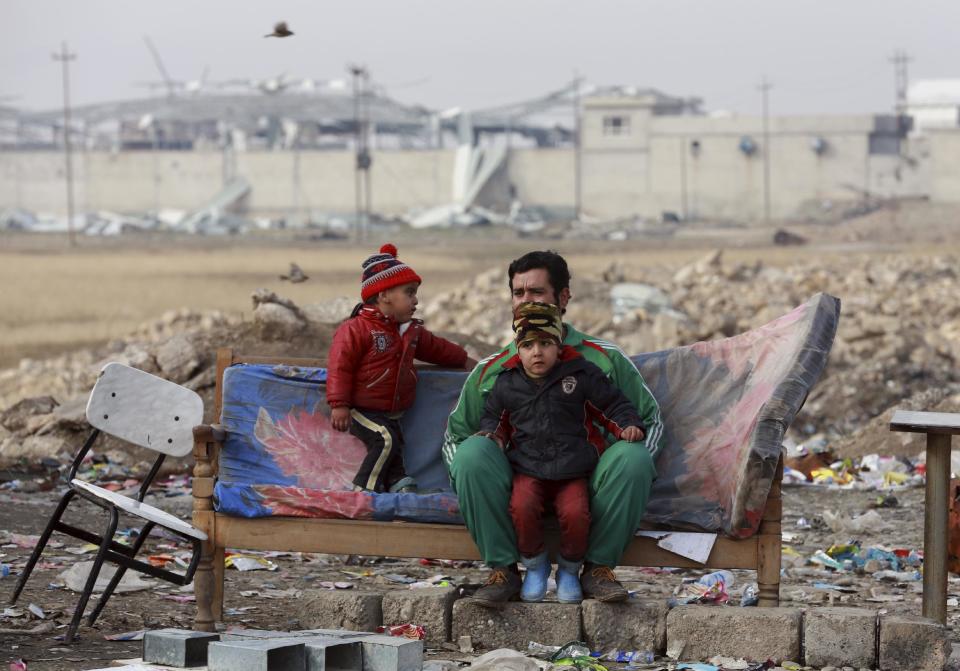 A displaced father and his children, who fled fighting between Iraqi security forces and Islamic State militants, waiting at the gathering point to be taken for a camp for internally displaced people, in Bartella, around 19 miles (kilometers), from Mosul, Iraq, Saturday, Dec 31, 2016. (AP Photo/ Khalid Mohammed)