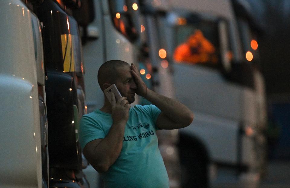 A driver of a freight lorry talk son his phone as he stands outside his cab parked at a truck stop off the M20 leading to Dover, near Folkestone in Kent, south east England on December 22, 2020, after France closed its borders to accompanied freight arriving from the UK due to the rapid spread of a new coronavirus strain. - The British government said Tuesday it was considering tests for truckers as part of talks with French authorities to allow the resumption of freight traffic suspended due to a new coronavirus strain. Britain was plunged into fresh crisis last week with the emergence of a fresh strain of the virus, which is believed to be up to 70 percent more transmissible than other forms. (Photo by JUSTIN TALLIS / AFP) (Photo by JUSTIN TALLIS/AFP via Getty Images)