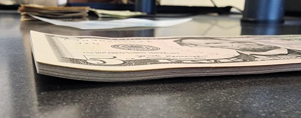 Stack of US five-dollar bills on a table with a blurry background of additional banknotes