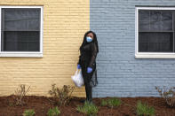 In this March 24, 2020, photo, Sharita Creel, of Washington, poses for a portrait holding a donated bag of groceries that she received in her community while wearing a mask and gloves in southeast Washington. Creel received the groceries from a neighborhood food delivery that is part of a new Martha's Table initiative, along with community partners, to get needed food directly to the neighborhoods they serve. Neighborhood volunteers are the tip of the spear for a grassroots community effort to keep Washington's most vulnerable neighborhoods fed during the unprecedented coronavirus crisis which has nearly shut down the American economy. (AP Photo/Jacquelyn Martin)