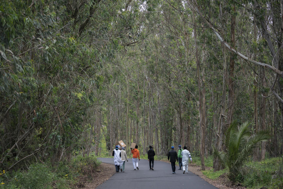 Migrants walk on a road carrying donated clothes by local residents to Las Raices camp in San Cristobal de la Laguna, in the Canary Island of Tenerife, Spain, Friday, March 19, 2021. While Spain has been critical of its European neighbours' lack of solidarity when it comes to sharing the responsibility of migration, the country is similarly being criticized by migrants, authorities and human rights organizations on the Canary Islands where some 23,000 people arrived by sea last year and where many thousands remain on the island forcefully. (AP Photo/Joan Mateu)