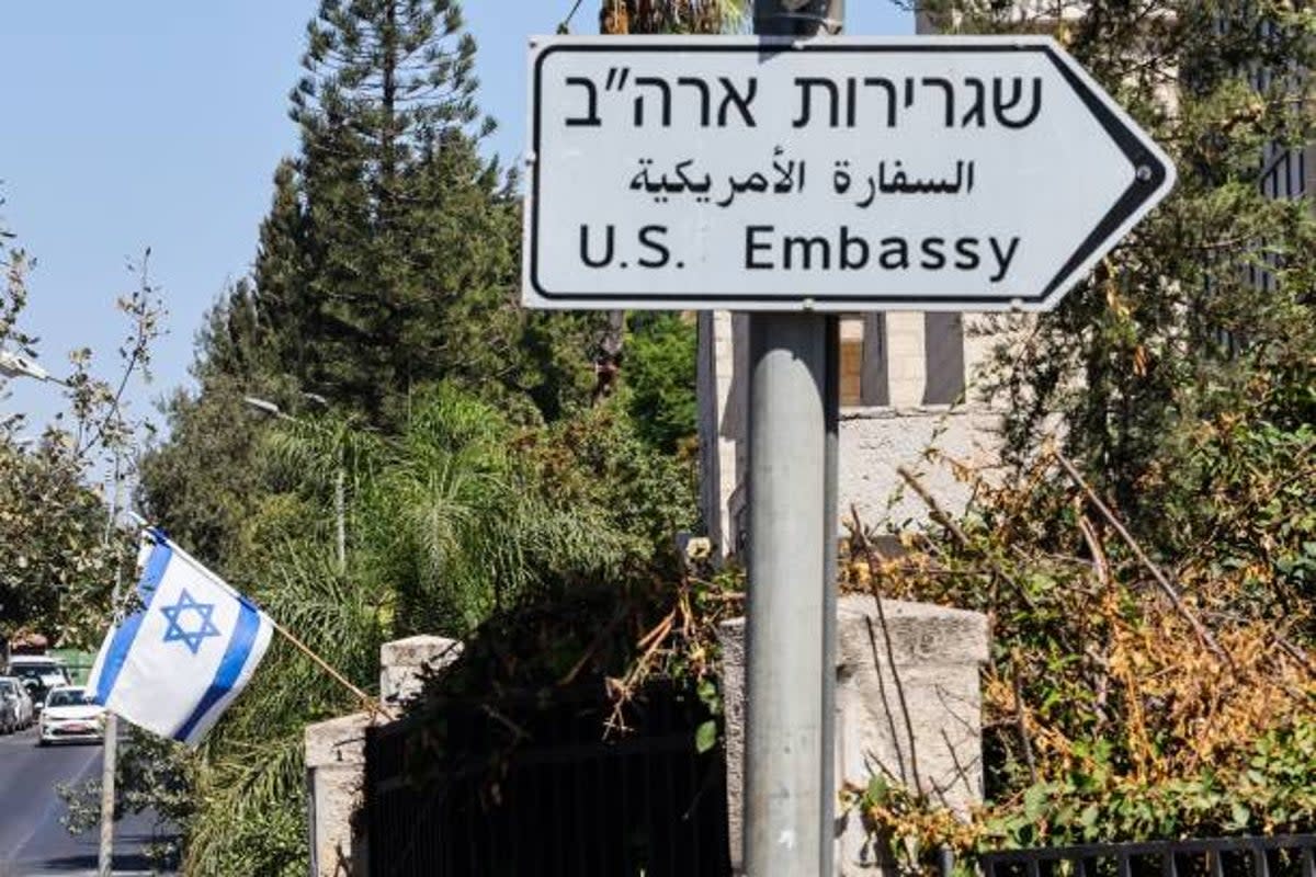 An Israeli flag is displayed in front of a building near a road sign for the US embassy in Jerusalem  (AFP via Getty Images)