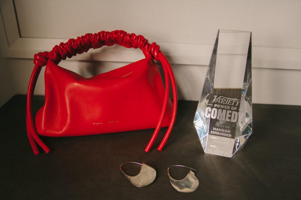 a red purse sitting beside a pair of earrings and a variety power of comedy award