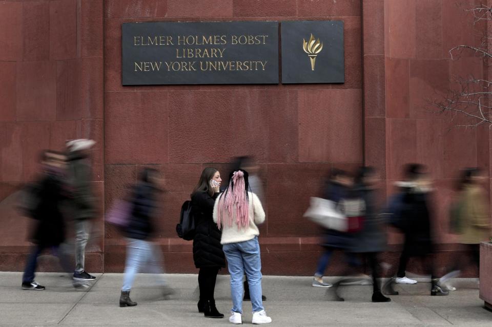 Two students pause while walking along Washington Square South in front of the Elmer Holmes Bobst Library at New York University, Wednesday, Dec. 14, 2016, in New York. New York University has introduced a program to help students save money by putting them up in elderly people's spare bedrooms. Participating students will pay $5,000 a year, thousands of dollars less than the cheapest on-campus housing option. Almost all of the money will go to their senior hosts. (AP Photo/Julie Jacobson)