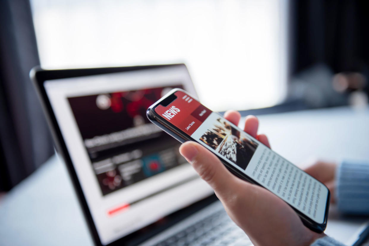 Person reading online news on a smartphone and laptop Getty Images/oatawa