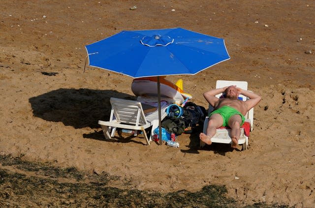 A man lying on a sun lounger on sand under a parasol