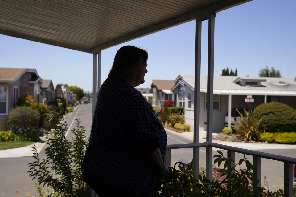 In this June 29, 2021, photo, Judy Pavlick, 74, stands on the patio outside where she lives at a mobile home park in Sunnyvale, Calif. Newly retired, Pavlick was among hundreds of seniors who enjoyed the low cost-of-living and friendly atmosphere at Plaza Del Rey, a sprawling mobile home park in Sunnyvale. Then the Carlyle Group acquired the property and things began to change. Pavlick's rent surged by more than 7%. Additional increases followed. She said the unexpected jump forced her and her neighbors, many on fixed incomes and unable to relocate, to sometimes choose between food and medicine. (AP Photo/Eric Risberg)