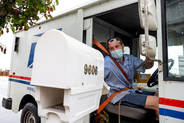 A USPS worker wearing a mask puts envelopes in a mailbox while driving past as the state of New Jersey continues Stage 2 of re-opening following restrictions imposed to slow the spread of coronavirus on August 13, 2020 in Ventnor City, New Jersey.