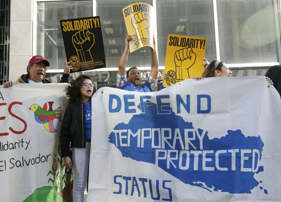 FILE - In this March 12, 2018 file photo, supporters of temporary protected status of immigrants cheer as they hold signs and banners with the outline of El Salvador at a rally at a federal courthouse in San Francisco. Immigrants from Honduras and Nepal have filed a lawsuit alleging the Trump administration unfairly ended a program that lets them live and work in the United States. The lawsuit filed late Sunday, Feb. 10, 2019, in federal court in San Francisco alleges that the U.S. Department of Homeland Security's decision to end so-called temporary protected status for the countries was motivated by racism. In 2018, a federal judge in San Francisco temporarily blocked the U.S. government from halting the program for immigrants from El Salvador, Haiti, Nicaragua and Sudan. The suit filed by citizens of those countries, much like this one, cited Trump's vulgar language during a meeting last year to describe African countries. (AP Photo/Jeff Chiu, File)