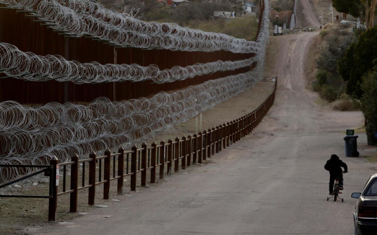 A boy rides his bike along a razor-wire-covered border wall that separates Arizona from Mexico - AP