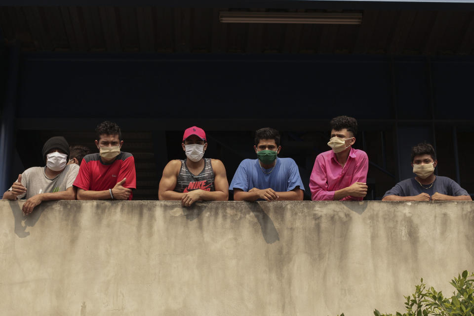 En esta foto del 4 de mayo de 2020, hombres portando cubrebocas miran hacia afuera de un edificio donde permanecen retenidos por haber roto una cuarentena decretada por el gobierno. (AP Foto/Salvador Meléndez)