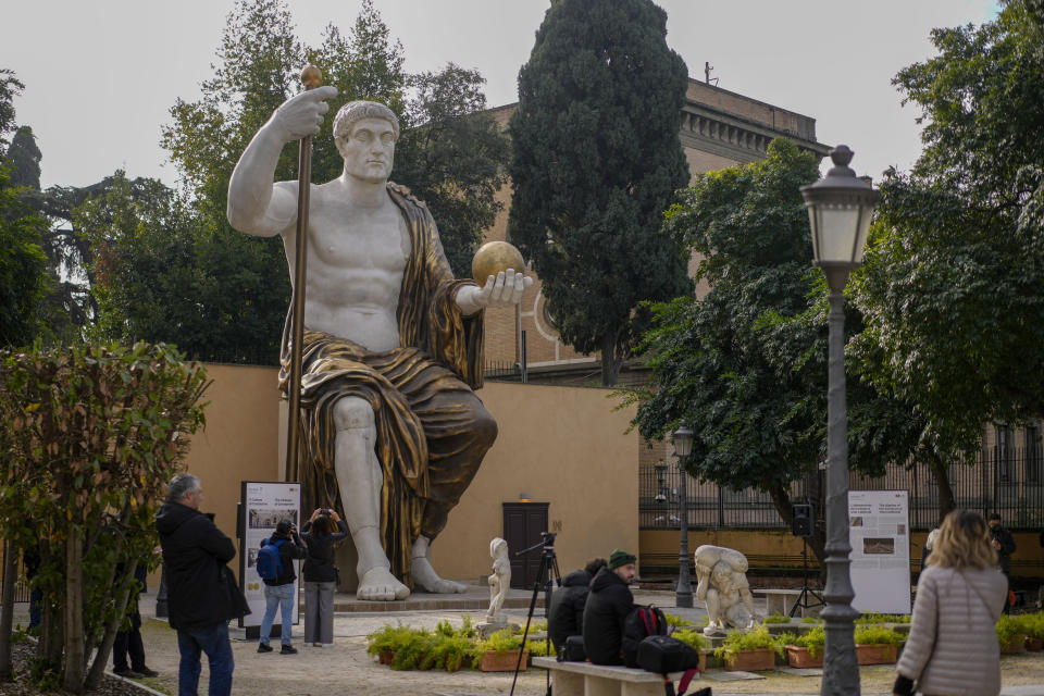 Visitors admire a massive, 13-meter (yard) replica of the statue Roman Emperor Constantine commissioned for himself after 312 AD that was built using 3D technology from scans of the nine giant original marble body parts that remain, as it was unveiled in Rome, Tuesday, Feb. 6, 2024. The imposing figure of a seated emperor, draped in a gilded tunic and holding a scepter and orb, gazing out over his Rome, is located in a side garden of the Capitoline Museums, just around the corner from the courtyard where the original fragments of Constantine's giant feet, hands and head are prime tourist attractions. (AP Photo/Andrew Medichini)