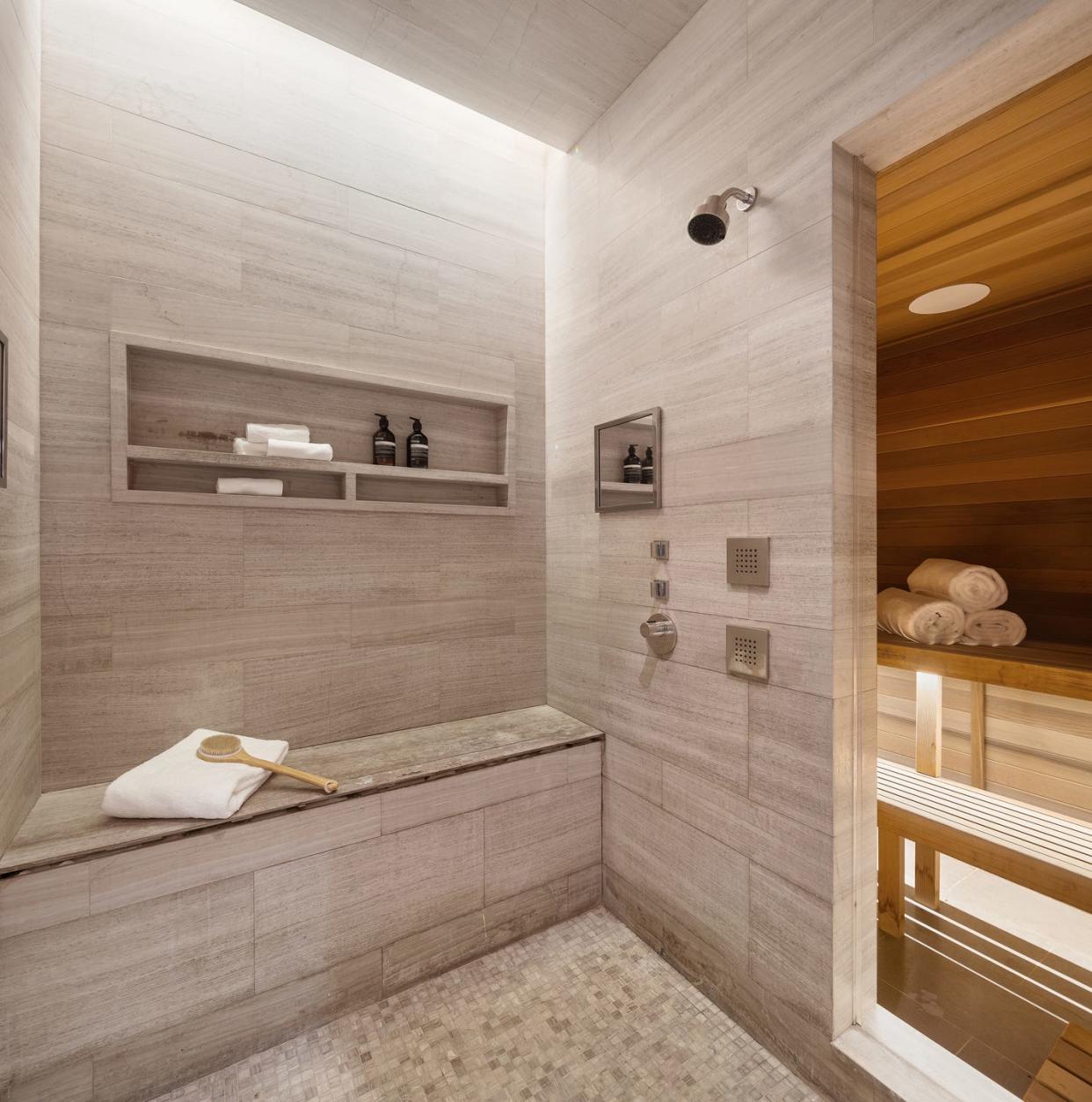 dry sauna with rolled up white towels in it, next to an open floor shower with a dry brush and towel on a built in bench