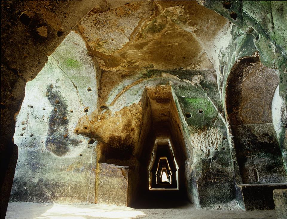 A photo of a long corridor made of rock leading forward towards a light source.