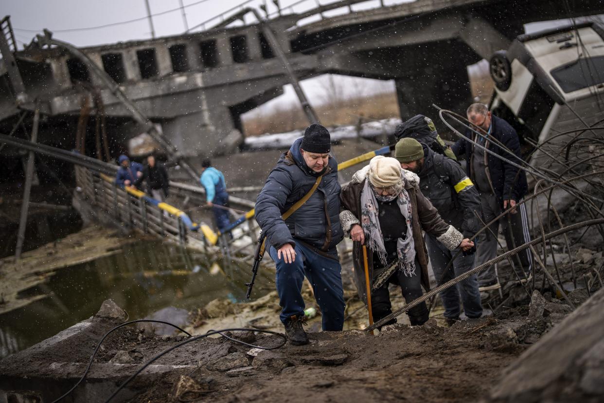 Local militiamen help an old woman crossing a bridge destroyed by artillery, as she tries to flee, on the outskirts of Kyiv, Ukraine, Wednesday, March 2, 2022.