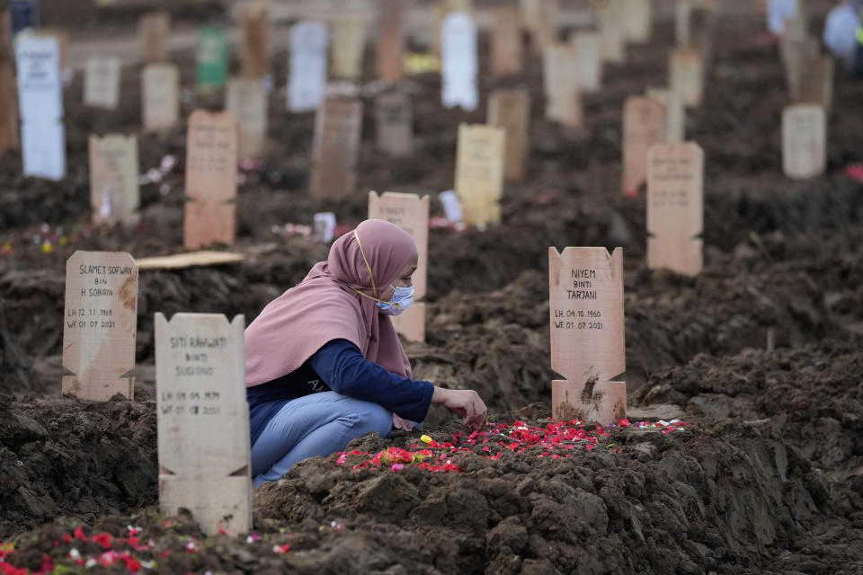 A woman sits at the grave of a relative who died of COVID-19 after her burial at Rorotan Cemetery in Jakarta, Indonesia, Thursday, July 1, 2021. Indonesian President Joko Widodo announced new community restrictions and the mobilization of the National Police and other resources as the world's fourth-most populous country has seen a rapid surge in COVID-19 cases in the last two weeks. (AP Photo/Dita Alangkara)