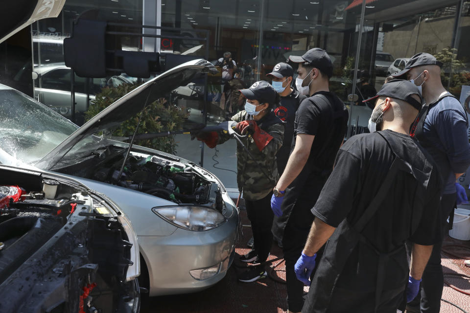 Female Iranian car detailer Maryam Roohani, left, cleans a car spraying water as her trainees watch, at a detailing shop in Tehran, Iran, Sunday, April 18, 2021. Roohani has battled skeptics and stereotypes to live out her dream of working as a professional detailer. The auto industry remains male-dominated around the world, let alone in the tradition-bound Islamic Republic. Still Iranian women, especially in the cities, have made inroads over the years. (AP Photo/Vahid Salemi)