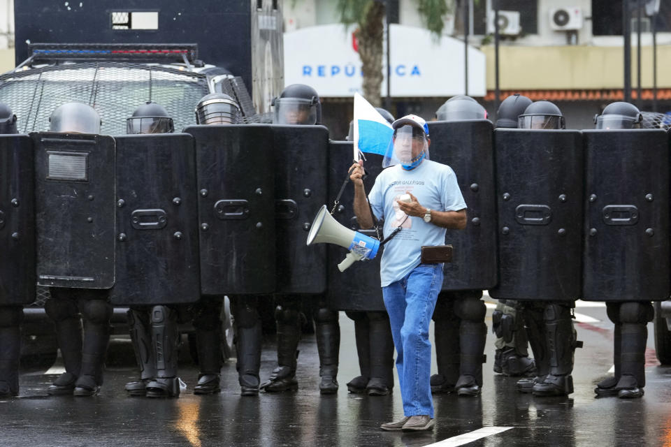 Un manifestante opuesto a un contrato minero con una empresa canadiense permanece junto a policías que impiden el acceso a la Asamblea Nacional, el viernes 20 de octubre de 2023, en Ciudad de Panamá. (AP Foto/Arnulfo Franco)