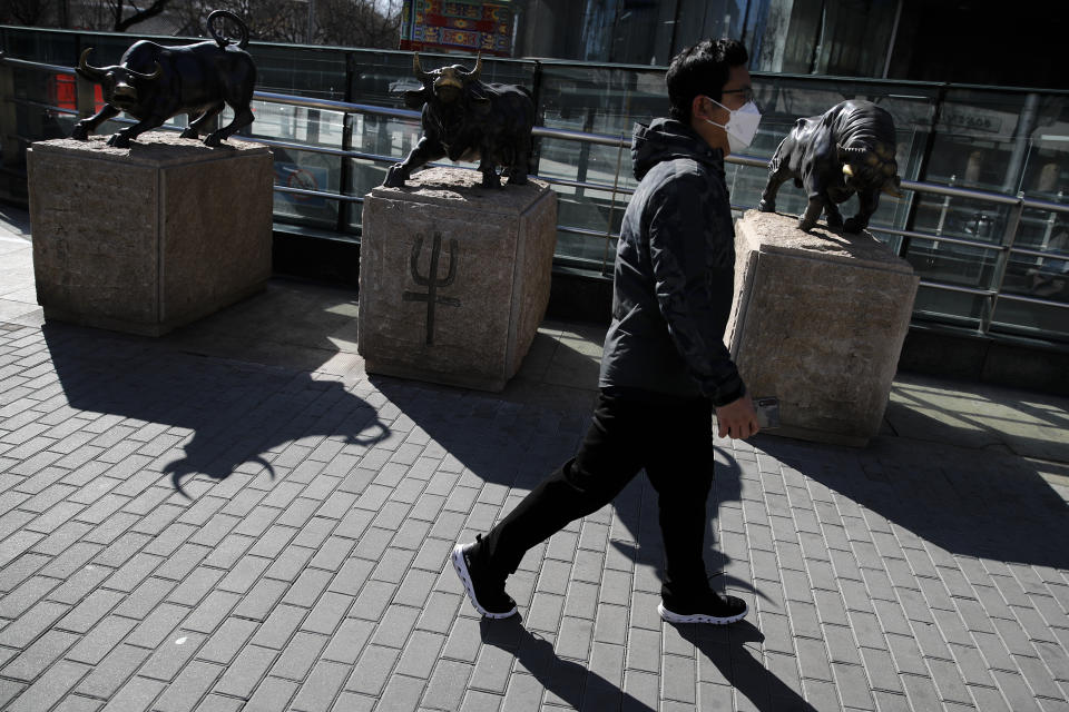 A man wearing a protective face mask walks by statues of bulls on display outside a bank in Beijing, Tuesday, March 10, 2020. Asian stock markets took a breather from recent steep declines on Tuesday, with several regional benchmarks gaining more than 1% after New York futures reversed on news that President Donald Trump plans to ask Congress for a tax cut and other quick measures to ease the pain of the virus outbreak. (AP Photo/Andy Wong)