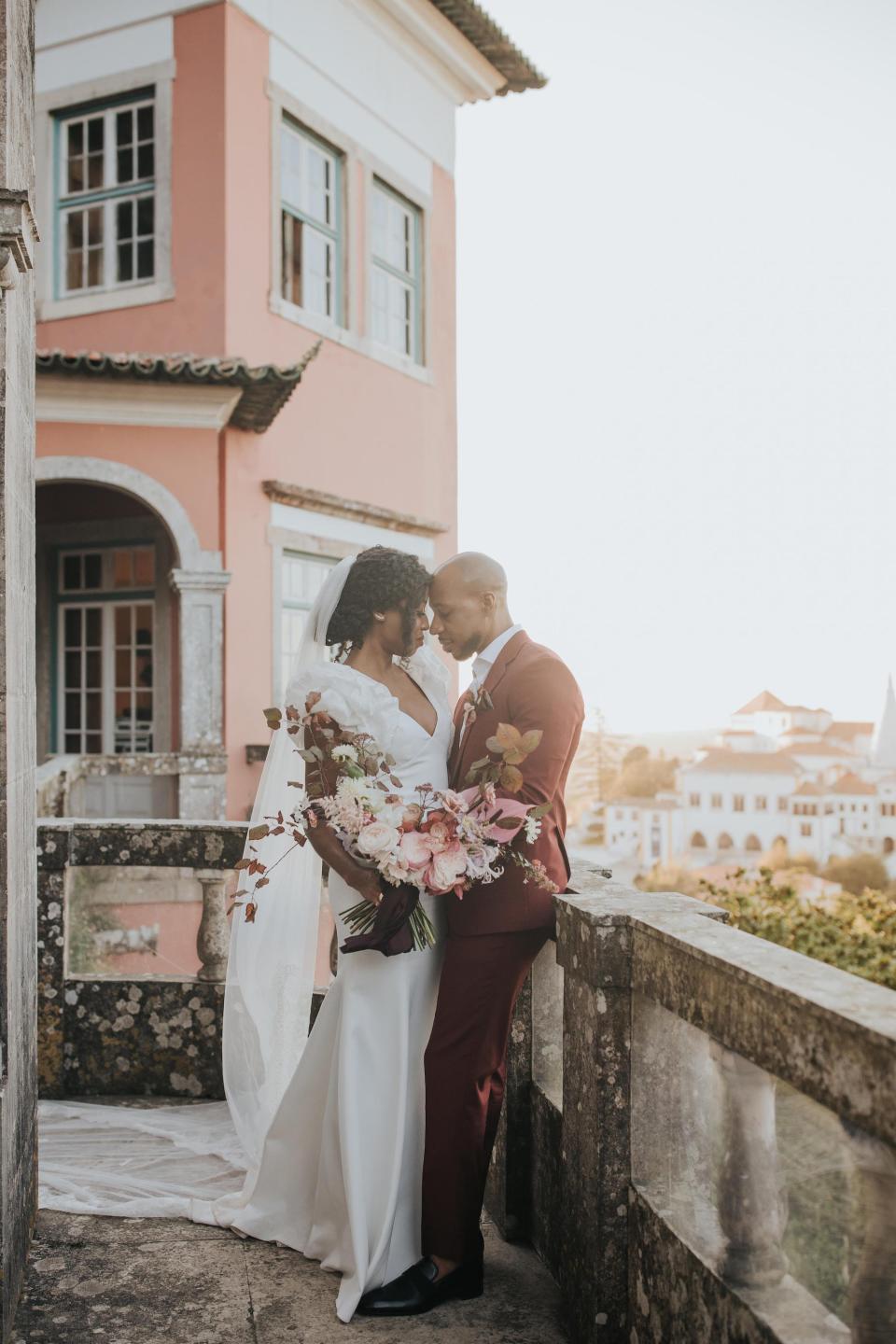 A bride and groom lean their heads together on a balcony.