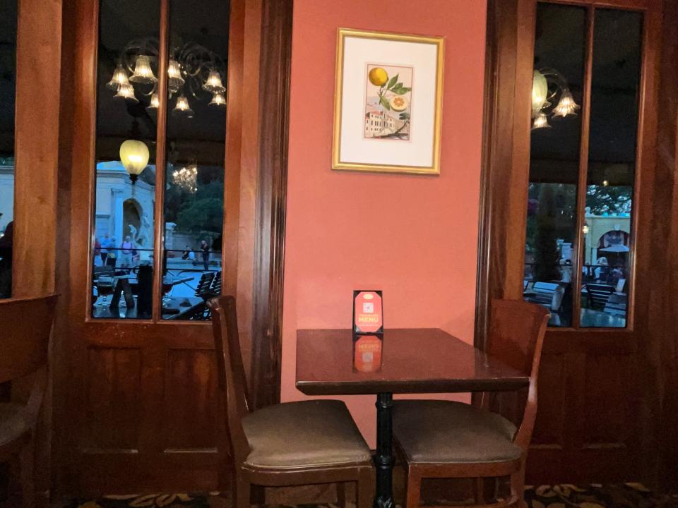 wooden table by orange wall with framed photo in the middle of two windows