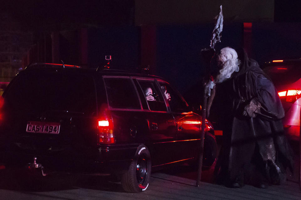 Visitors take photos from inside their cars of an actor at the Hopi Hari horror theme amusement park, in the Vinhedo suburb of Sao Paulo, Brazil, Friday, Sept. 4, 2020. Due to the restrictions caused by COVID-19, the park created a drive-thru tour that allow the public to enjoy the experience by car. (AP Photo/Carla Carniel)