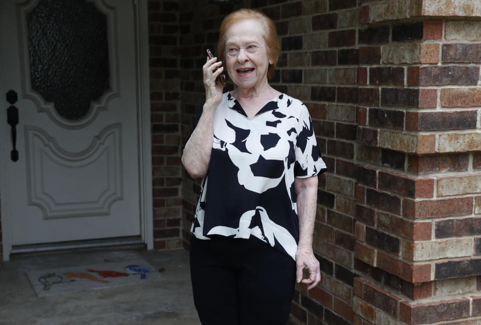 Dell Kaplan, 81, talks on her phone if front of her home in Plano, Texas Friday, May 15, 2020. For Kaplan, the offer to get calls from a stranger just to chat while staying home during the coronavirus pandemic was immediately appealing. "It gets pretty lonely here by yourself," said Kaplan, a suburban Dallas resident who has been missing meals out with friends, family get-togethers and going to classes at a nearby college. The program being offered by the city of Plano is among those that have popped up across the U.S. during the pandemic to help older adults with a simple offer to engage in small talk. (AP Photo/LM Otero)