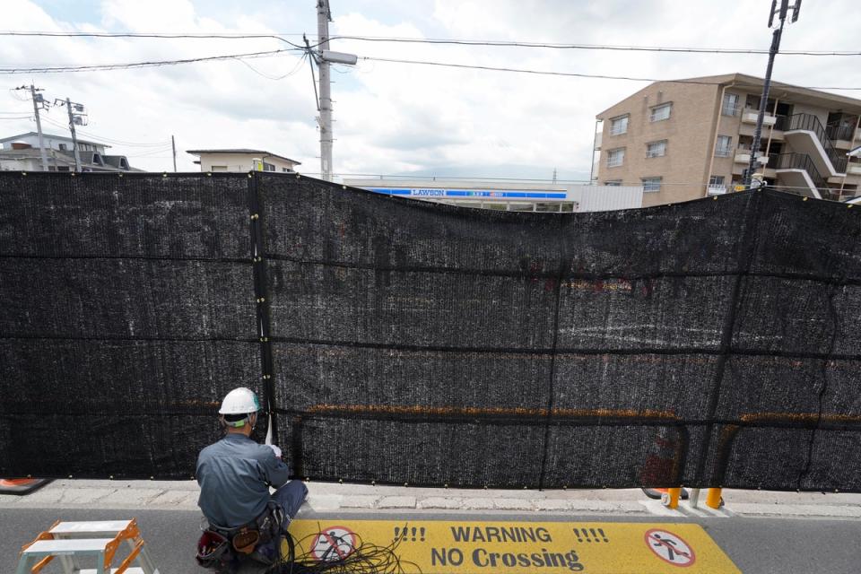 A worker installs a black shading net on the opposite side of the Lawson Kawaguchiko Ekimae convenience store in Fujikawaguchiko (EPA)