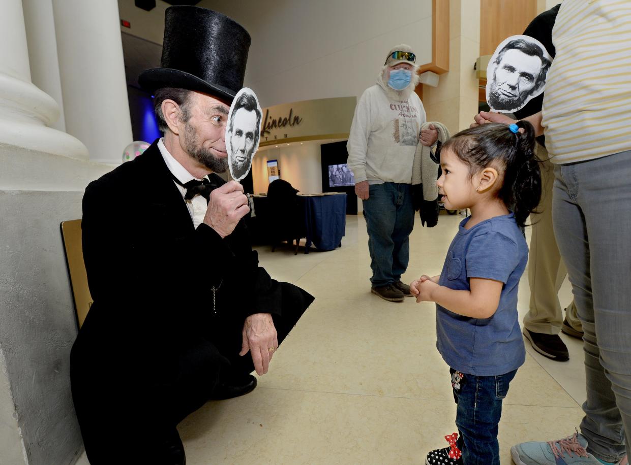 Lincoln impersonator Fritz Klein of Springfield, left, holds a fan in front of his face with Lincoln's image while talking with Daniela Rodriguez, 2, of Springfield at the Abraham Lincoln Presidential Library and Museum Saturday Feb. 11, 2023. The museum was holding several events to celebrate Lincoln's birthday Sunday.