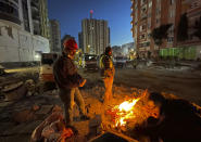 People try to stay warm around a fire as rescuers search in a destroyed building in Adana, southeastern Turkey, Thursday, Feb. 9, 2023. Tens of thousands of people who lost their homes in a catastrophic earthquake huddled around campfires in the bitter cold and clamoured for food and water Thursday, three days after the temblor hit Turkey and Syria.(AP Photo/Lefteris Pitarakis)