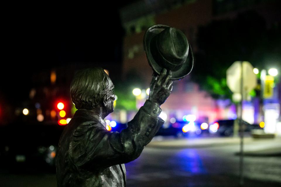 A statue of Irving Weber is seen in the foreground as Iowa City Police officers investigate the scene of a shooting early Sunday, May 14, 2023, at the corner of Gilbert Street and Iowa Avenue in Iowa City, Iowa.