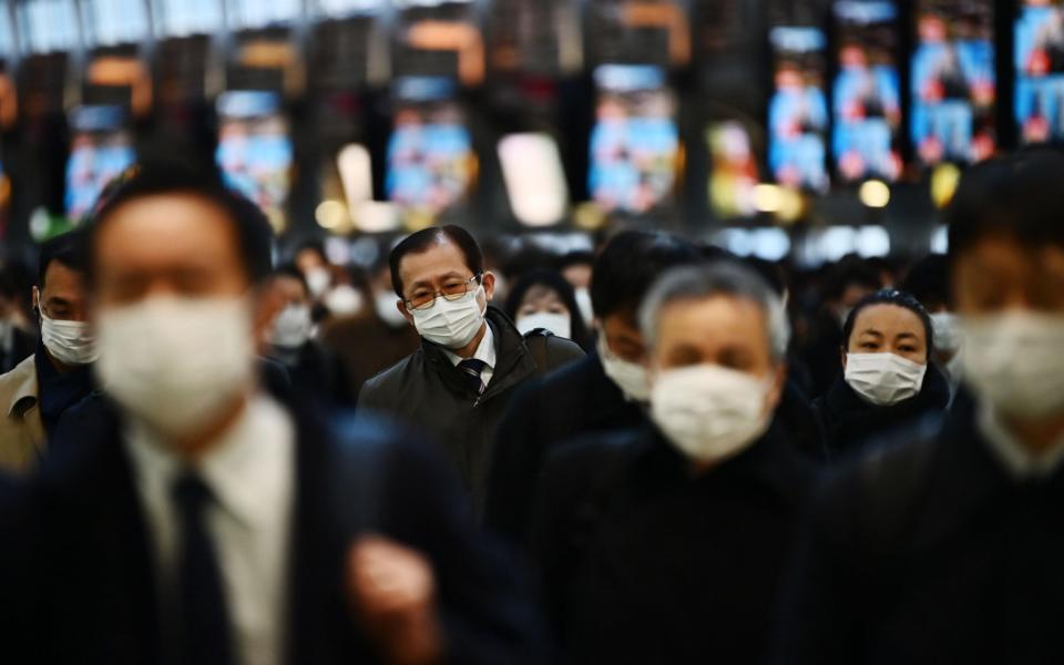 Mask-clad commuters make their way to work during morning rush hour at the Shinagawa train station in Tokyo - AFP