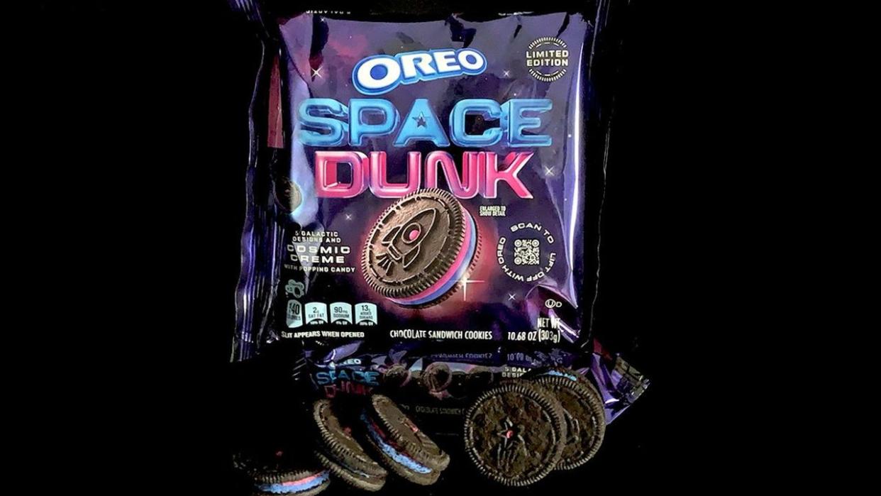  A container of oreo cookies featuring pink and purple icing inside and a rocket design stamped on them. 